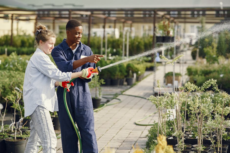 Two young gardeners work together watering plants in an outdoor garden setting.