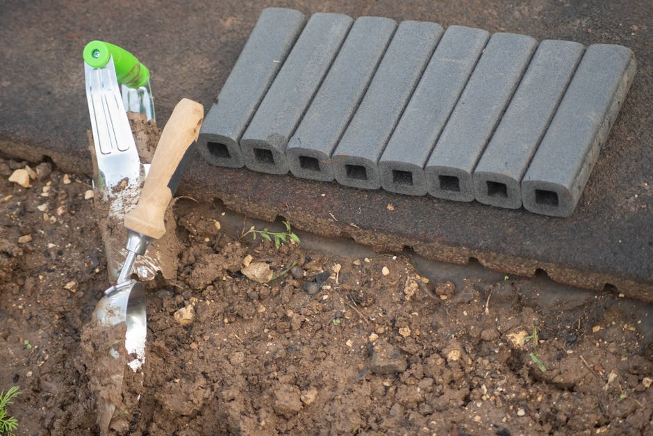 Close-up of a trowel and garden pavers next to soil in a garden setting.